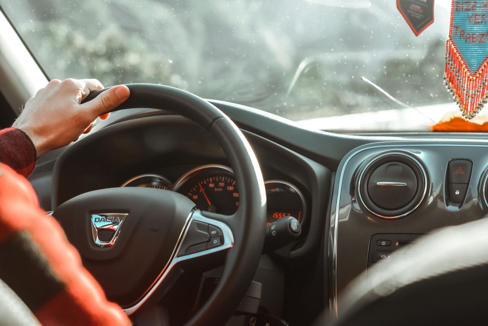 Close-up of a driver's hand resting on a car steering wheel with the dashboard behind